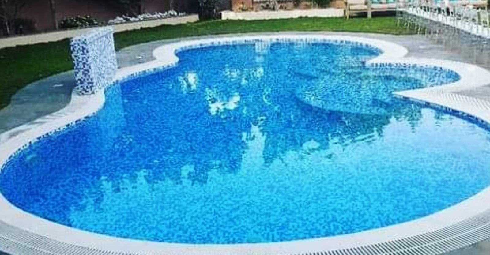 Kidney-shaped mosaic swimming pool surrounded by lawn